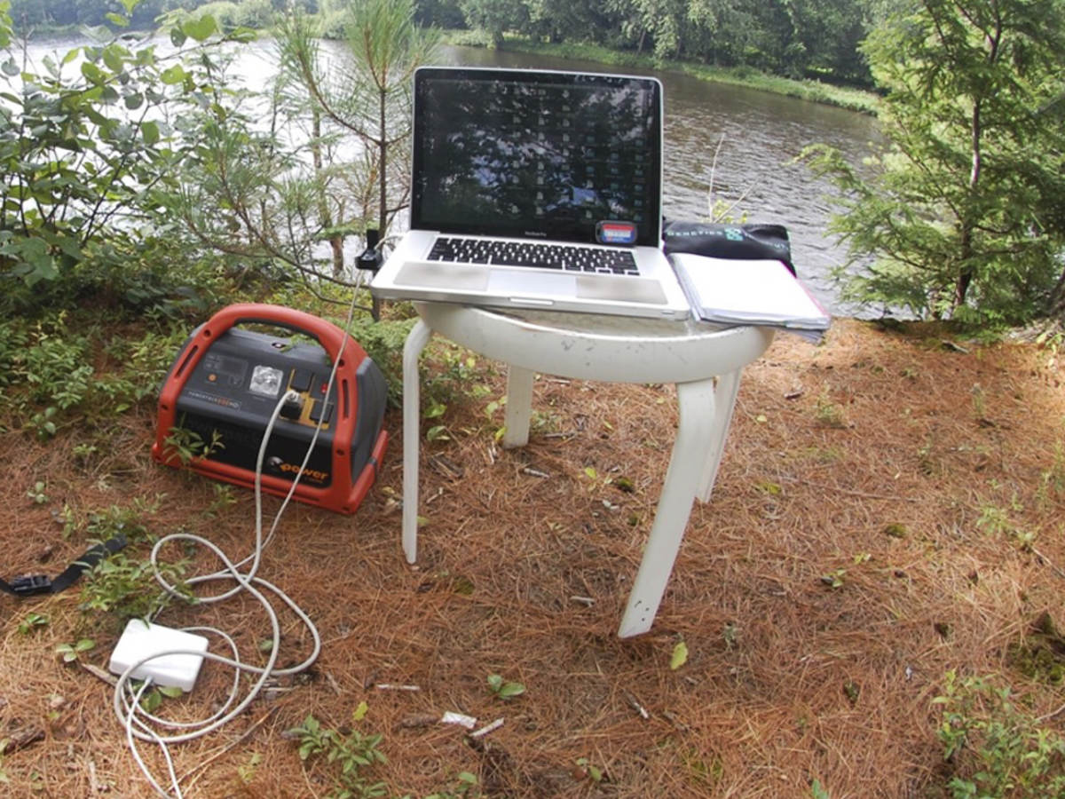 Portable power pack connected to laptop in a nature scene.